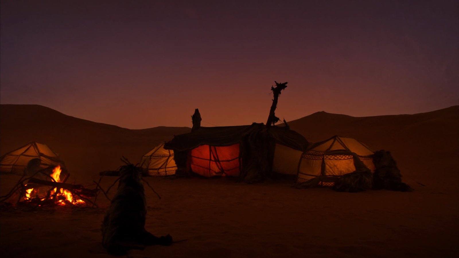 A traditional Berber desert camp glowing warmly at dusk with a campfire in front