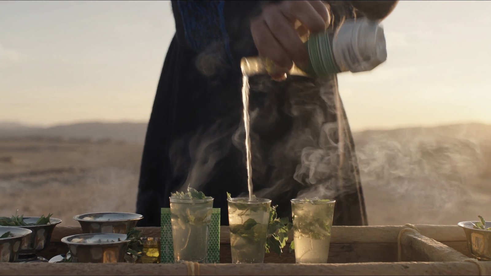Mint tea poured from height into small glasses at a desert camp, steam rising