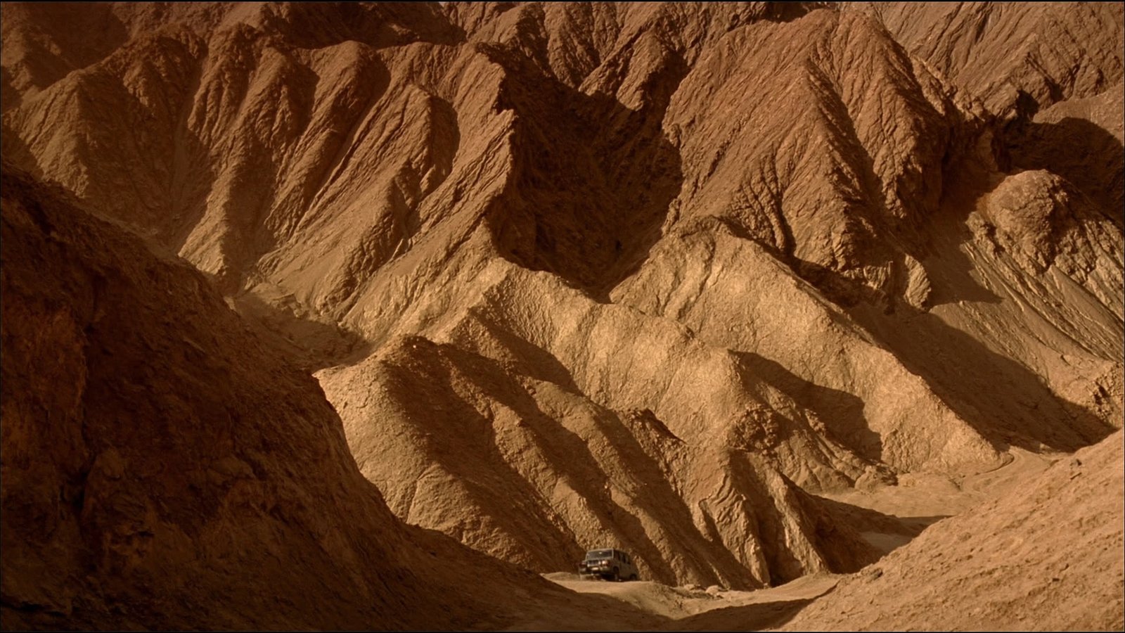 A 4x4 winding through the rugged ochre rock formations of the Tajine Mountains
