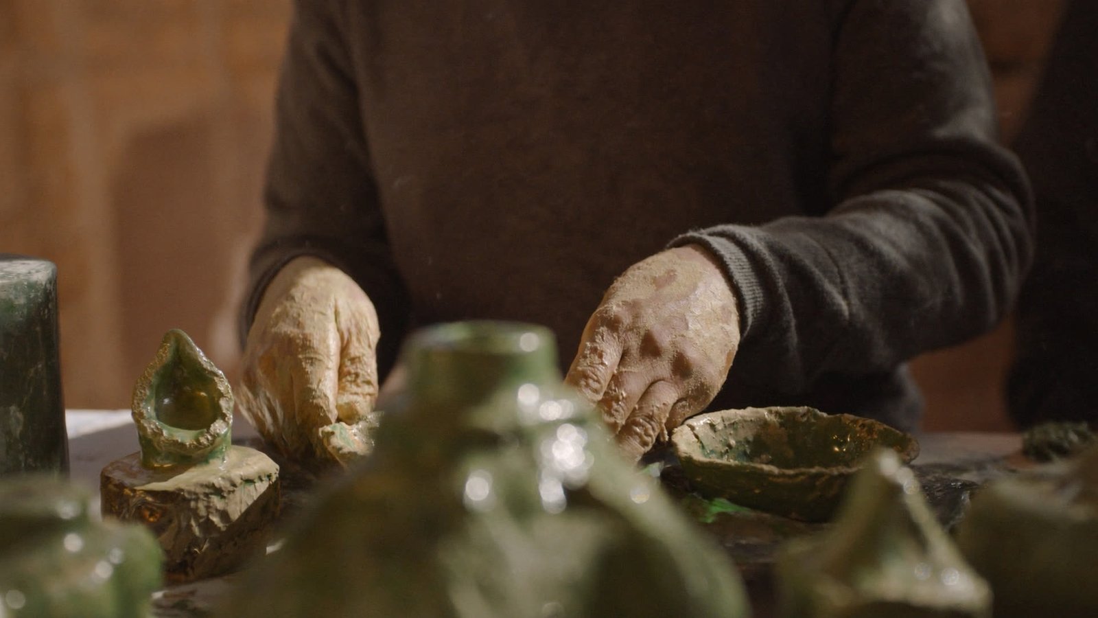 A potter's hands shaping green-glazed ceramics in a traditional Tamgroute workshop